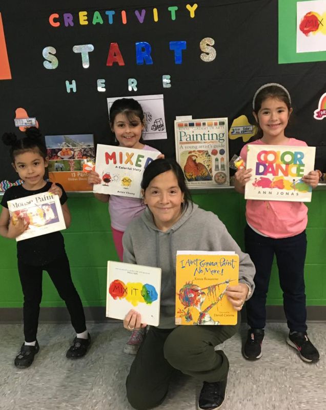 A group of student and a teacher holding up colorful books.