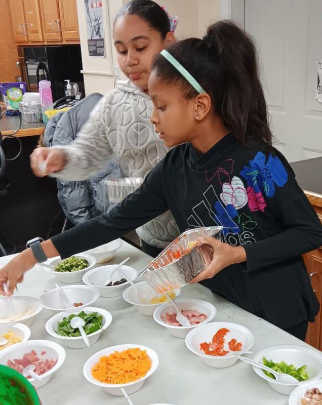 Two girls in a culinary class placing ingredients into bowls. 