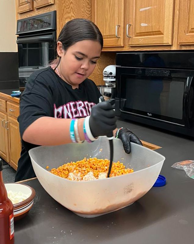 A girl in a culinary class mixing a bowl of corn. 